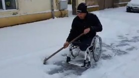 Exemplu de atitudine civică: Un bărbat în scaun cu rotile își deszăpezește trotuarul din fața casei